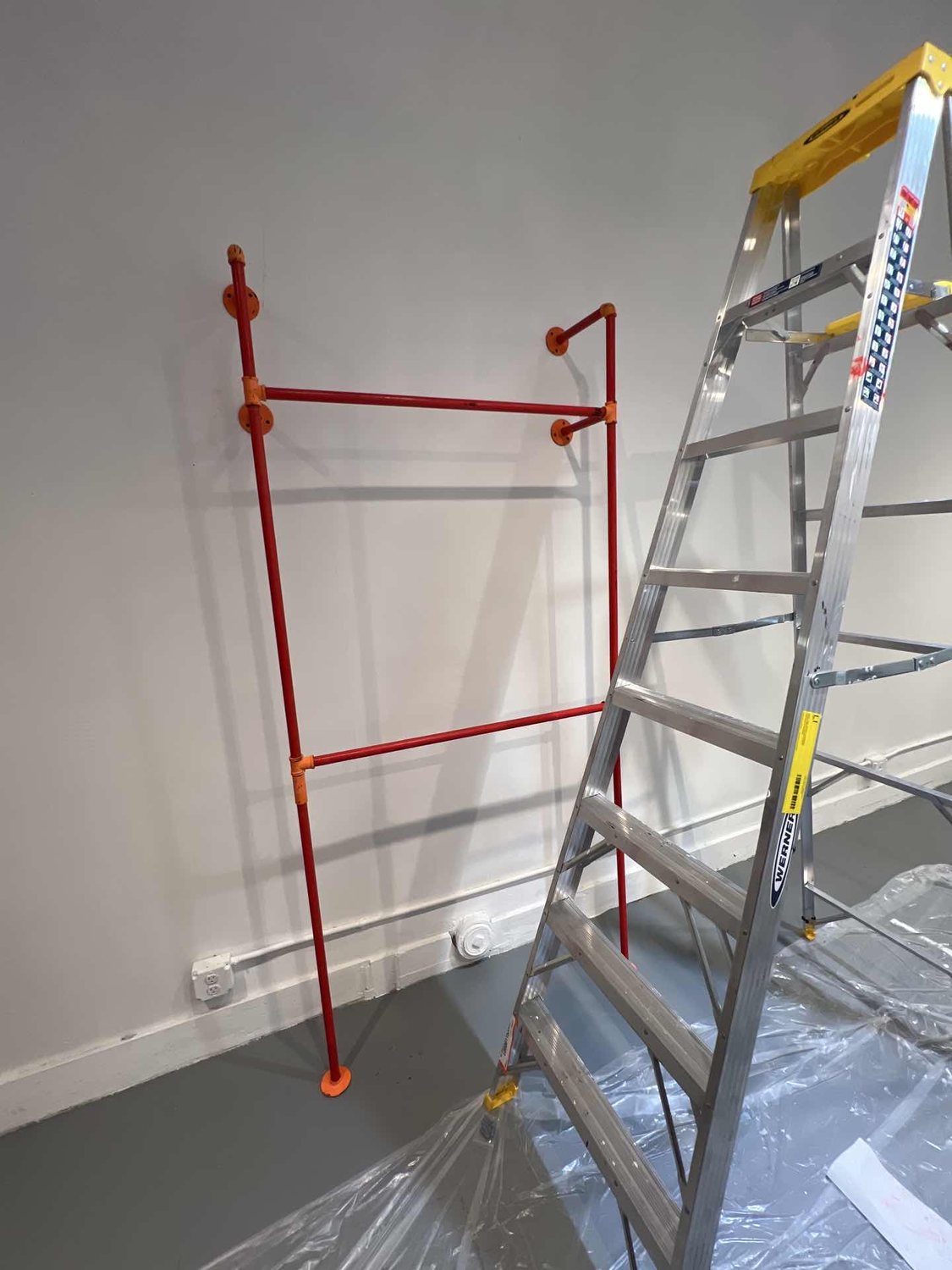 During the build: a red steel rack fixed to the bare wall, ladder and dust sheet on the floor