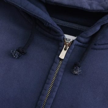 Macro detail of the navy hoodie: hood opening, knotted drawcords, the metal zip head and the woven brand label at the neck