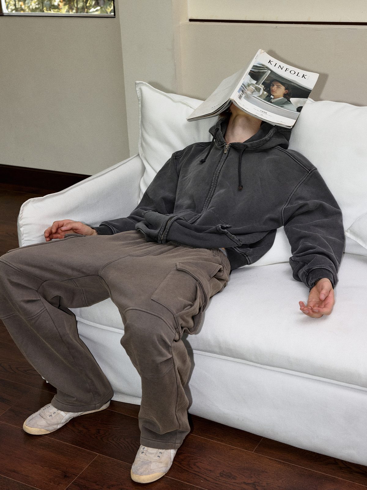 Graphite hoodie worn on a white sofa with brown trousers
