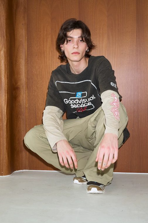 Layered-sleeve tee worn crouching, showing the sleeve join above the elbow
