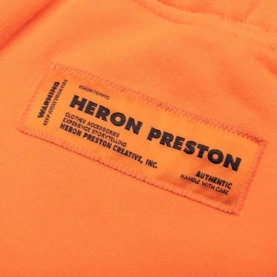 A Heron Preston care label sewn onto orange jersey, set as industrial warning type
