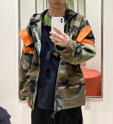 The camo jacket worn open, strap across the chest