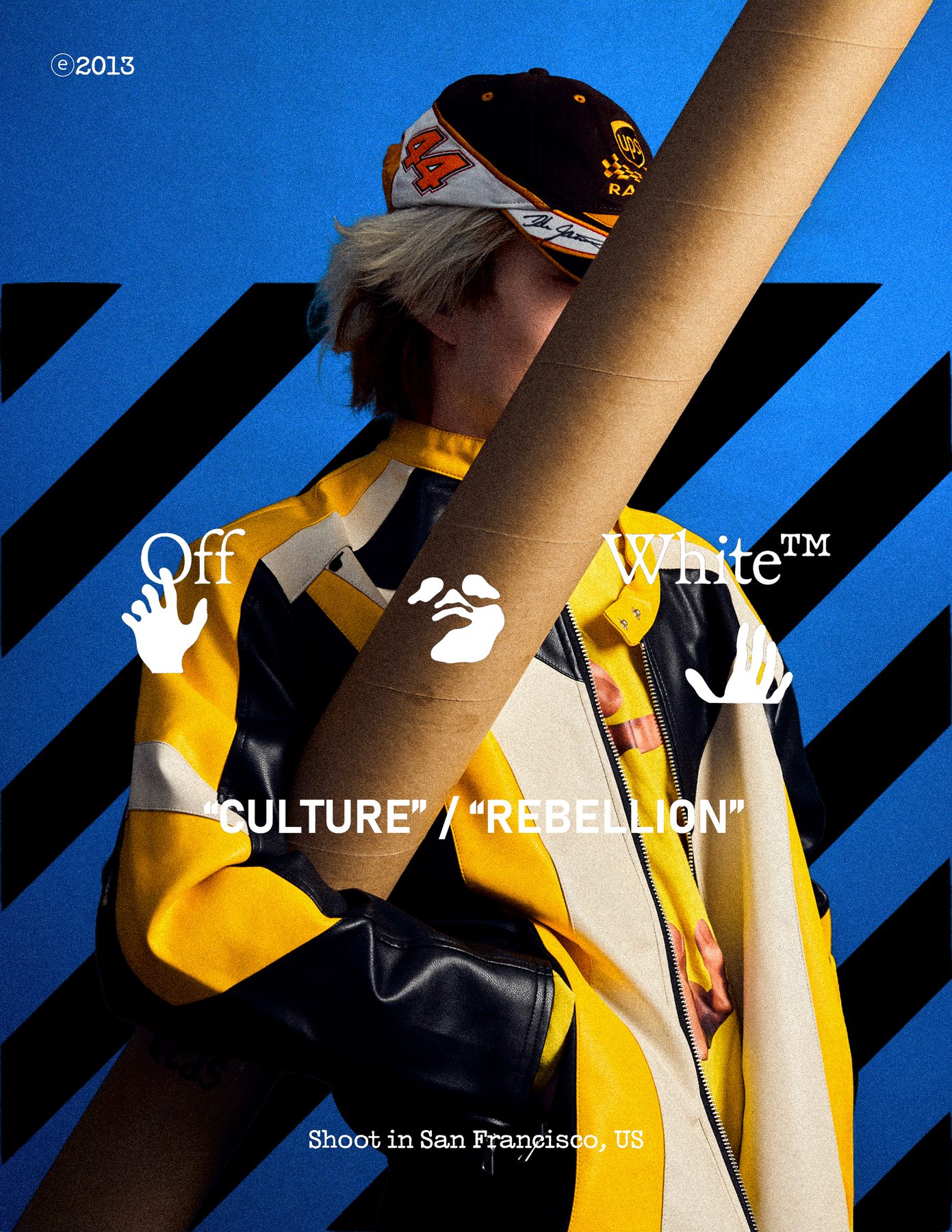 Model holding a mailing tube diagonally across the frame against blue and black stripes