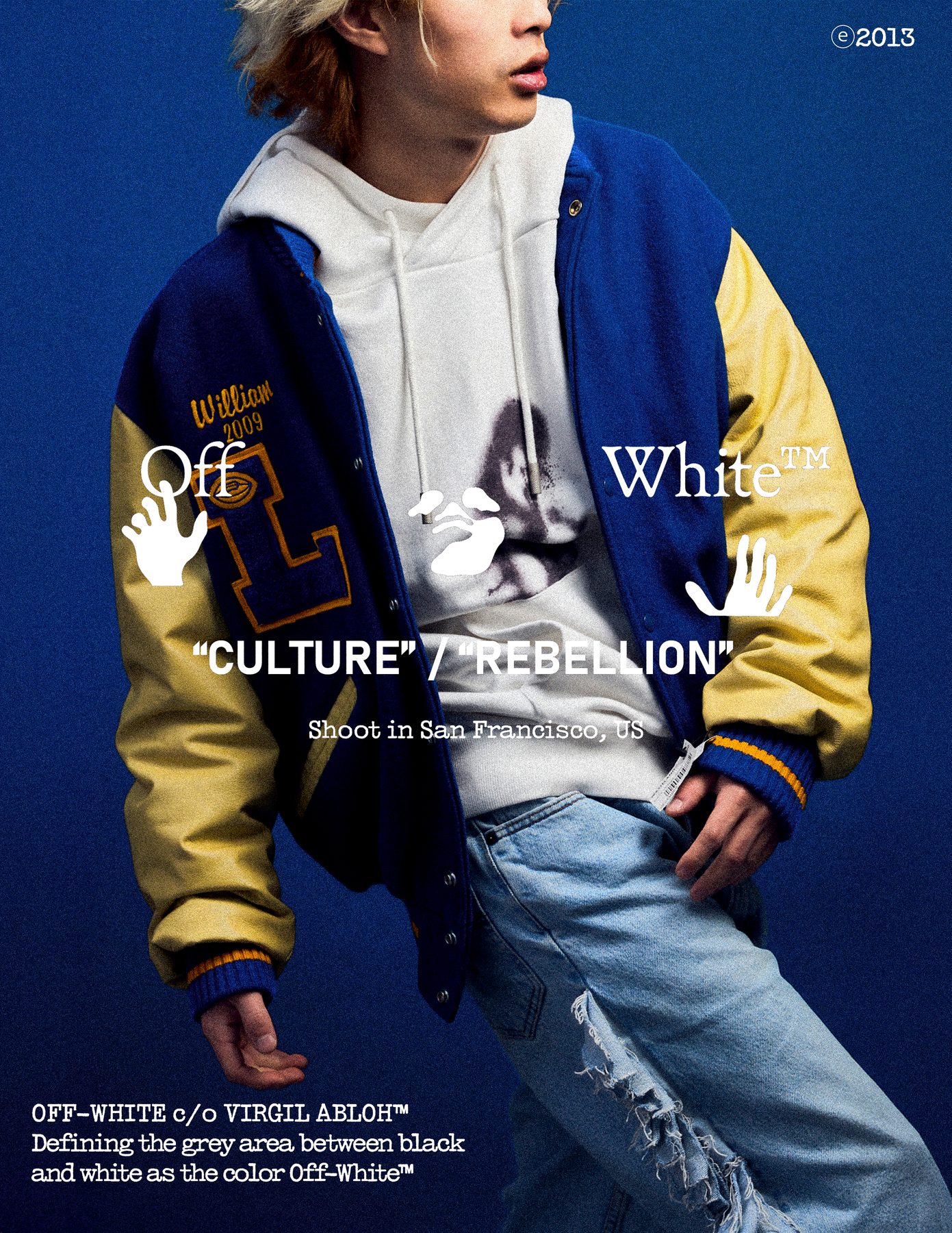 Model in a blue and yellow varsity jacket over a white hoodie against a blue ground