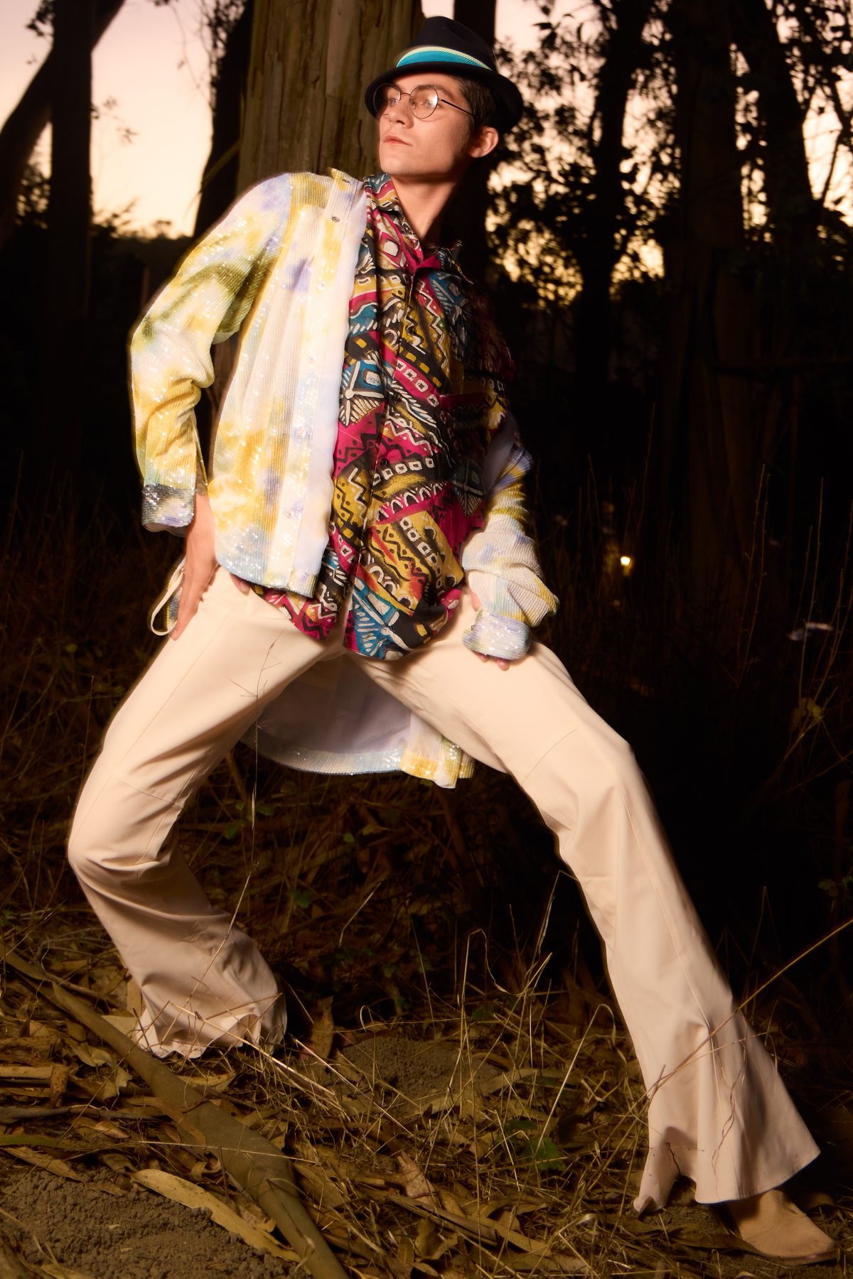 Sequinned jacket, hands on hips, flash against a dark treeline
